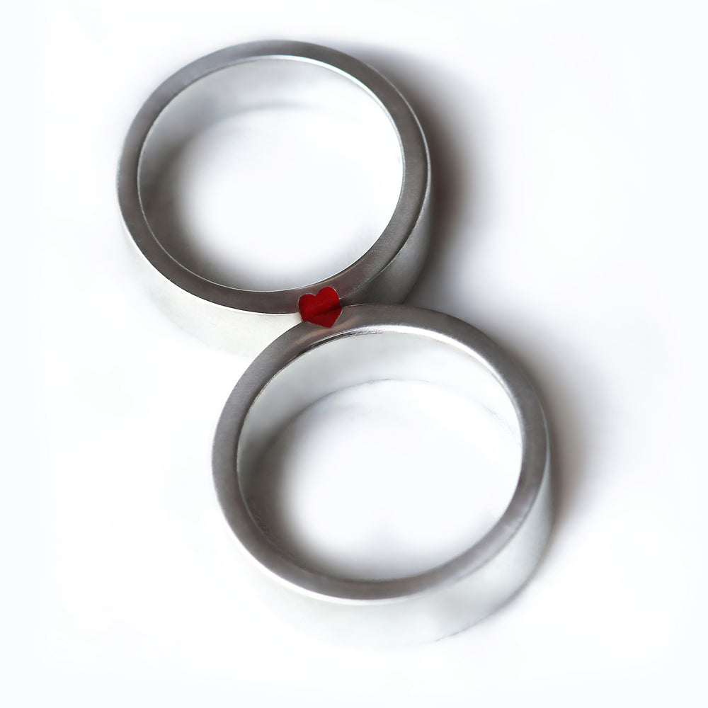 Two 18K white gold wedding rings with a matte brushed finish, featuring a vertical red enamel stripe on the face of each band.