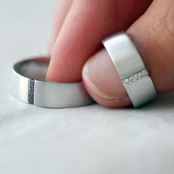 Hand holding matching black and white Diamond engagement rings